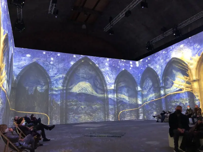 En uppslukande utställning där Van Goghs konstverk projiceras på väggarna, vilket ger en känsla av att van Gogh är levande. Besökare sitter och njuter av den visuella upplevelsen.