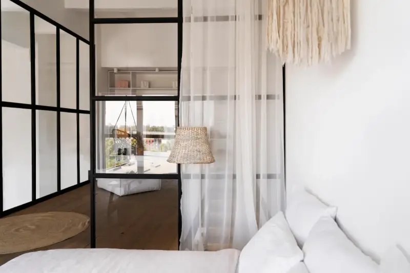 Verre et métal séparent la chambre en deux, avec une seule fenêtre offrant une vue sur l'extérieur. Un rideau léger ajoute de la douceur.