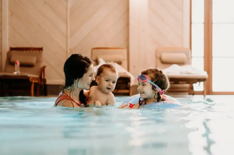 Rodzina cieszy się basenem w hotelu dla dzieci w Wiśle. Mama z dwójką dzieci pluska się w wodzie, tworząc radosne wspomnienia.