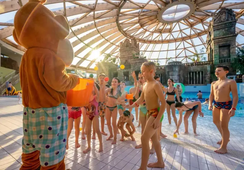 Maskotka rzuca piłeczki dzieciom w aquaparku w Budapeszcie. Radosna zabawa pod szklaną kopułą.