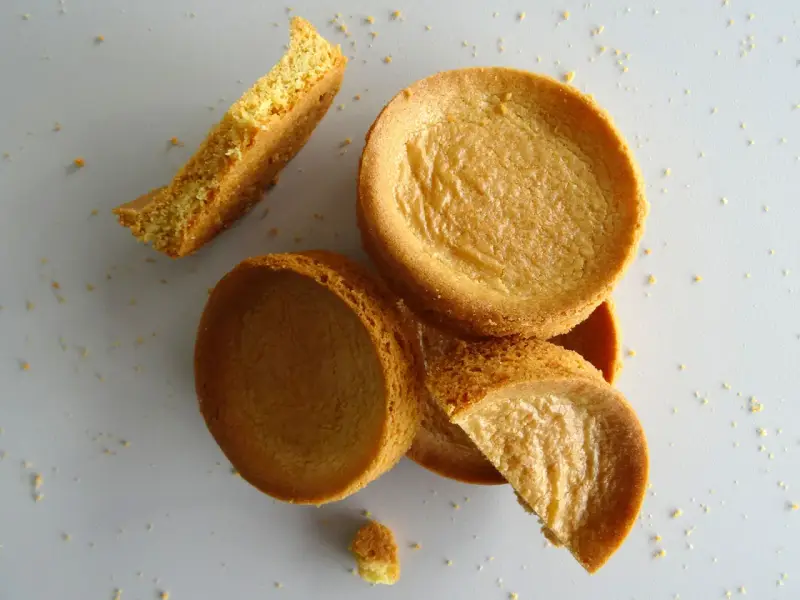 Des morceaux de sablé breton dorés, certains entiers, d'autres brisés, éparpillés sur un fond clair.