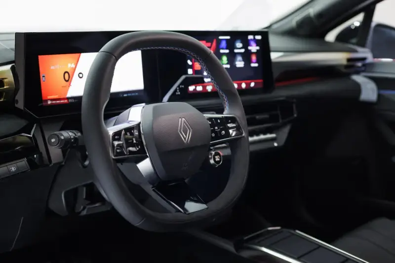 Volante e cruscotto digitale con schermi moderni, dettagli blu e logo Renault. Interni della nuova Clio 2026.