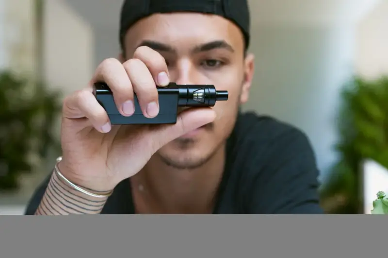 Joven con gorra negra sostiene un cigarrillo electrónico, mostrando sus claromizadores.