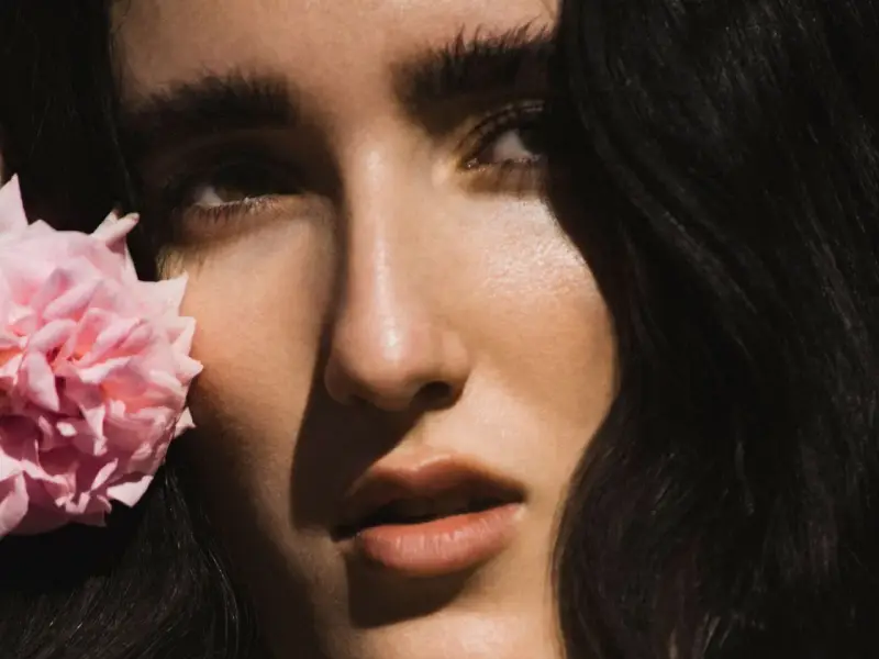 Primer plano de Judeline, cantante, con una flor rosa junto a su rostro.