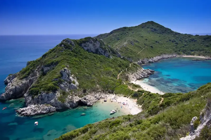 Malownicza zatoka z turkusową wodą i piaszczystą plażą, otoczona zielonymi wzgórzami. Tak właśnie wygląda Korfu, grecka wyspa, gdzie leży ten raj.