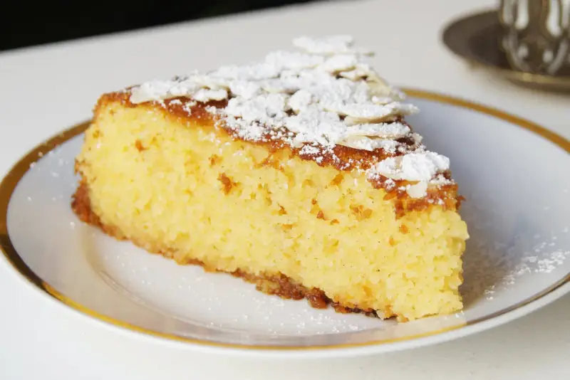 Rebanada de tarta de almendra esponjosa, espolvoreada con azúcar glas y láminas de almendra.