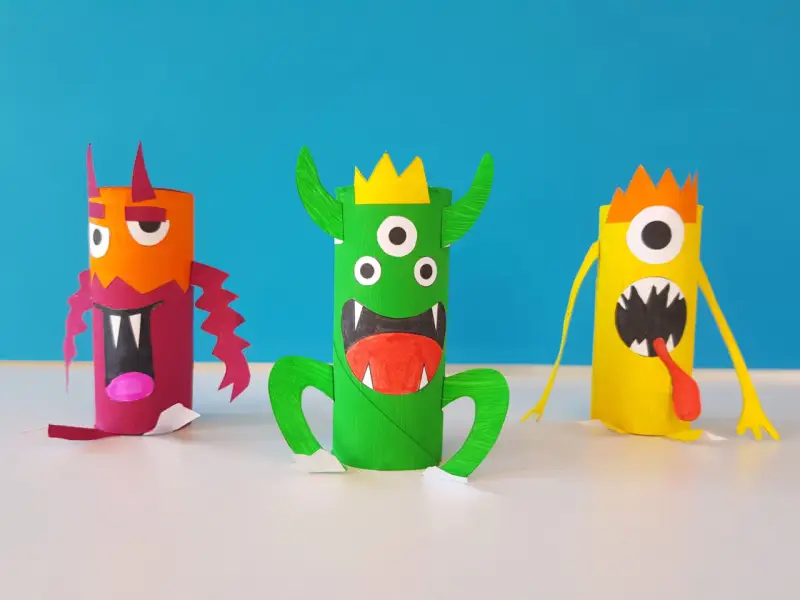 Trois monstres colorés faits à la main, en rouleaux de papier toilette, sur fond bleu.
