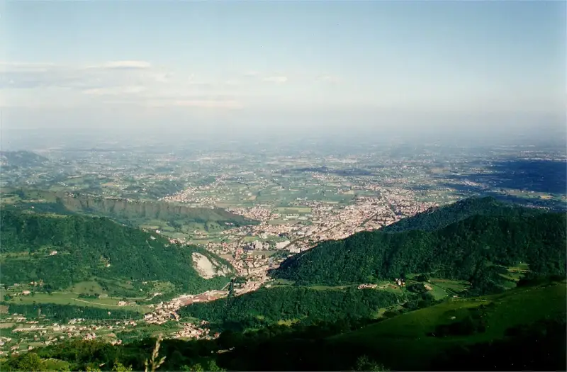 Vista panoramica dalla sella di Fadalto su una vasta pianura punteggiata di case e campi, con colline verdi in primo piano.