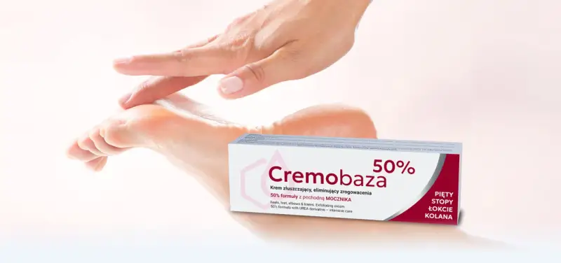 Dłoń delikatnie dotyka stopy, obok opakowanie kremu Cremobaza 50%. Produkt z mocznikiem, który pomaga zwalczać zrogowacenia.