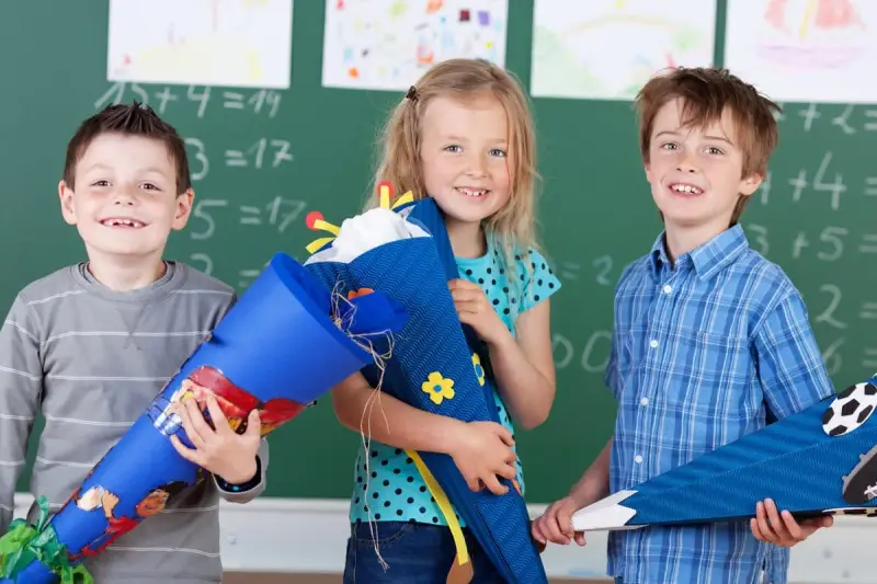 Drei Kinder mit Schultüten vor einer Tafel. Die Einschulung in Sachsen-Anhalt 2025 wird hier fröhlich gefeiert.