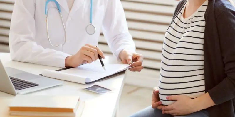 Lekarz omawia z ciężarną pacjentką kolejne trymestry ciąży, notując coś na dokumentach.