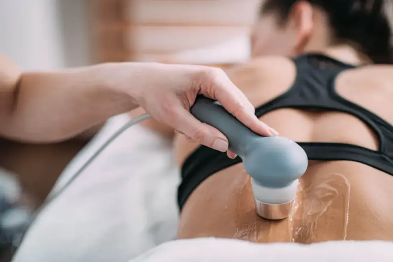 Therapeutin führt Ultraschall Physiotherapie am Rücken einer Patientin durch. Gel auf der Haut für die Behandlung.