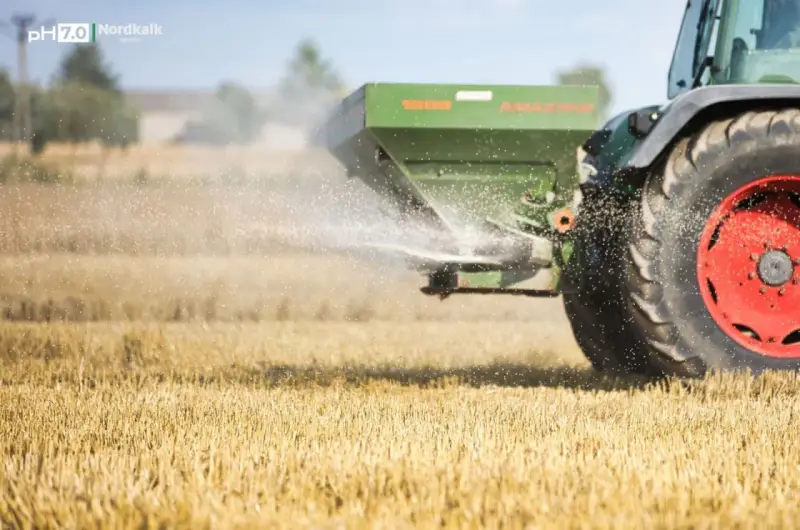 Traktor rozsiewa wapno magnezowe na polu.