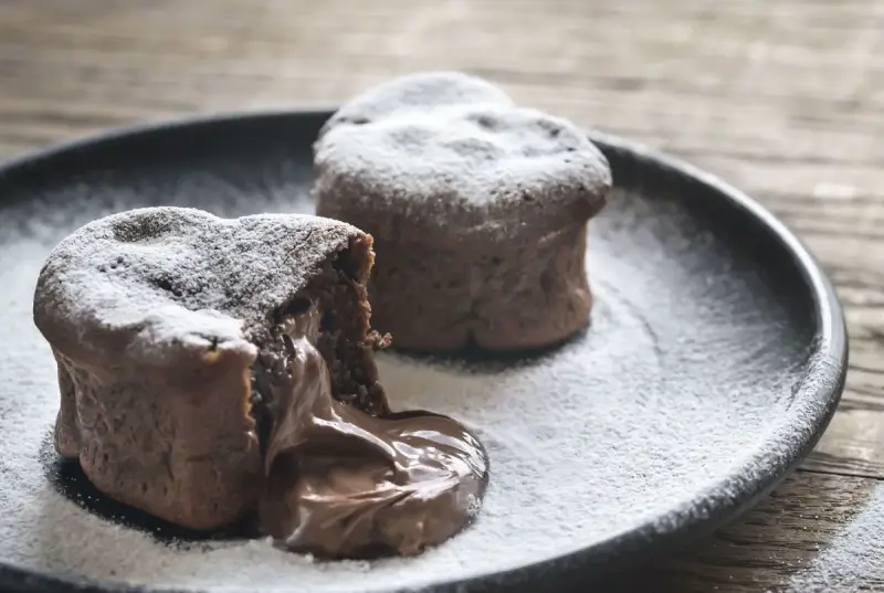 Deux coulants au chocolat inratables, saupoudrés de sucre glace, avec un cœur fondant qui déborde sur l'assiette.