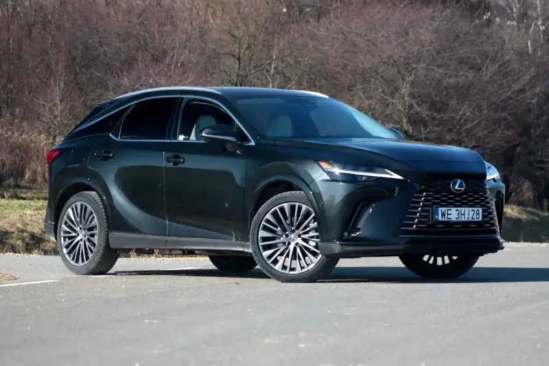 Ciemnozielony Lexus 450h z eleganckimi felgami stoi na drodze, otoczony suchymi krzewami.