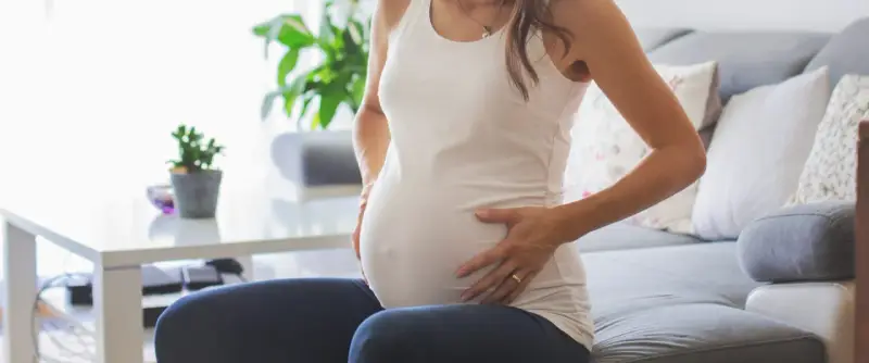 Kobieta w ciąży siedzi na kanapie, dotykając brzucha. Zauważyła brązowe plamienie w ciąży, co ją martwi.