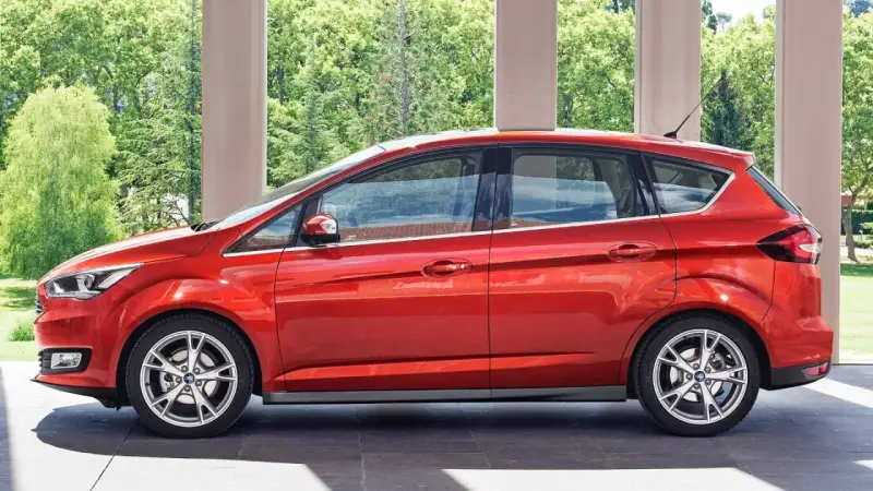 Czerwony Ford C-Max 1.6 benzyna zaparkowany pod arkadami, z zielenią w tle.