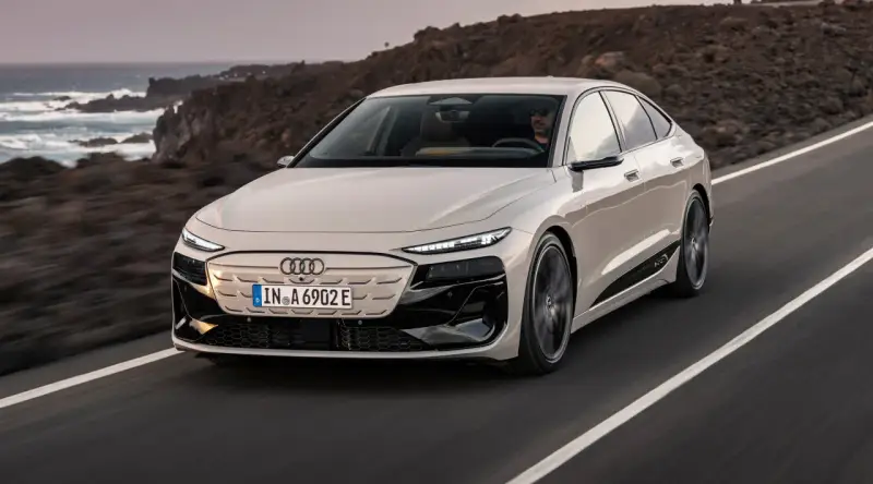 Jasnoszary Audi A6 e-tron jedzie po drodze z widokiem na ocean i góry.
