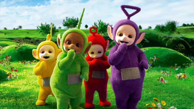 Teletubisie imiona: Tinky Winky, Dipsy, Laa-Laa i Po stoją na zielonej łące pełnej kwiatów.