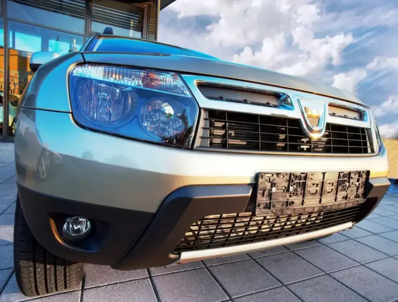 Złoty Dacia Duster 1.6 benzyna z chromowanym grillem i niebieskimi reflektorami, gotowy na przygodę pod błękitnym niebem.