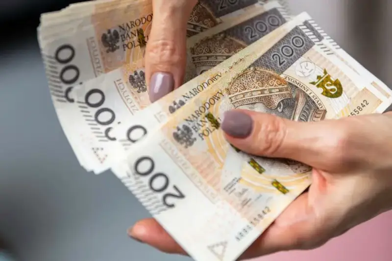 Dłoń trzyma stos banknotów 200 zł. To może być pożyczka od rodziny na nieprzewidziane wydatki.