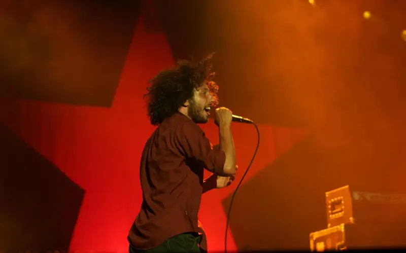 Zac Zack de la Rocha śpiewa z pasją na koncercie Rage Against the Machine. Czerwona gwiazda w tle podkreśla energię występu.