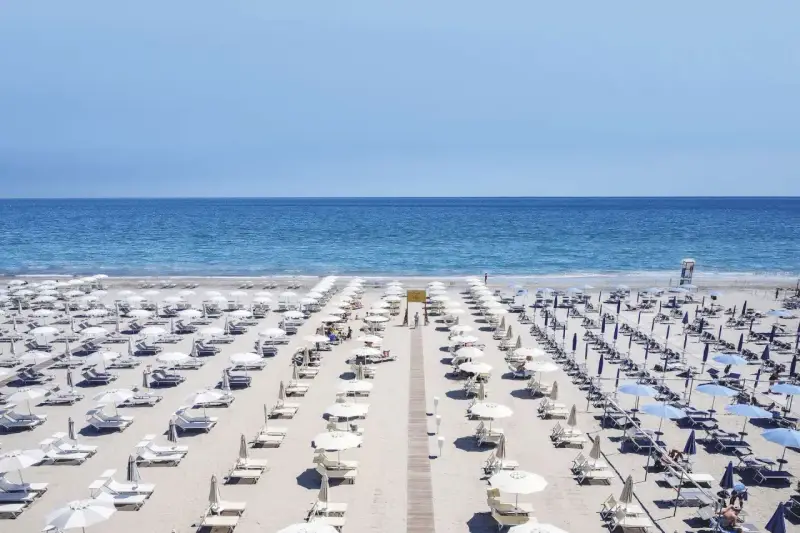 File di ombrelloni bianchi e lettini ordinati sui **stabilimenti balneari Cervia**, con il mare azzurro sullo sfondo.