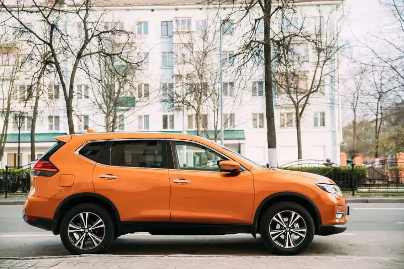 Pomarańczowy SUV do 50 tys. zaparkowany na tle białego budynku i drzew.