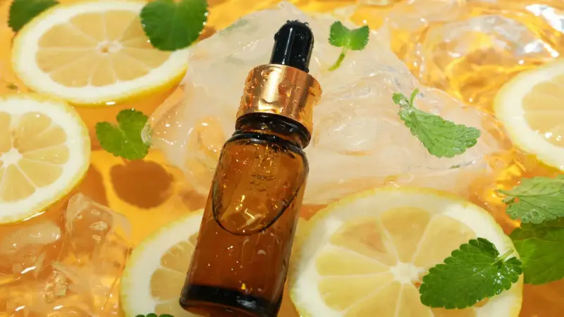 Kwas cytrynowy wzór: brązowa buteleczka z pipetą, plasterki cytryny, kostki lodu i listki mięty w bursztynowym płynie.