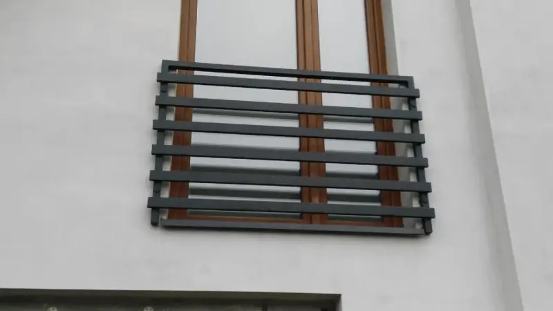 Nowoczesne balkony francuskie z ciemnoszarymi, poziomymi barierkami na tle białej ściany i brązowych okien.