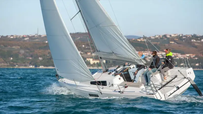 Bateau à voile "First 27" en pleine navigation, équipage concentré sur le plan d'eau bleu.