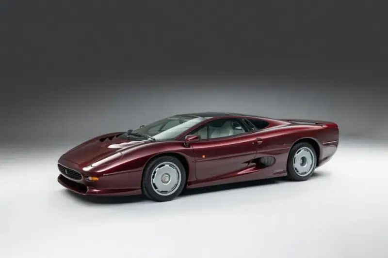 Bordowy Jaguar XJ220, ikona motoryzacji lat 90., prezentuje swoje aerodynamiczne linie na tle szarego tła.