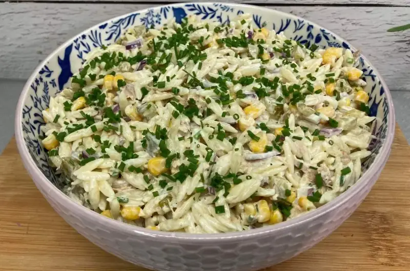 Pyszna sałatka z tuńczykiem, makaronem orzo, kukurydzą i szczypiorkiem, podana w ozdobnej misce.