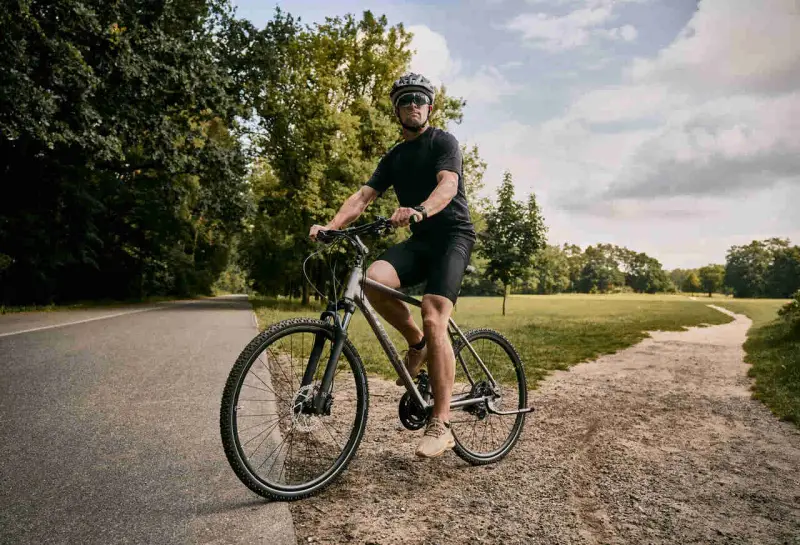 Mężczyzna w kasku i okularach jedzie na rowerze typu cross po ścieżce w parku.