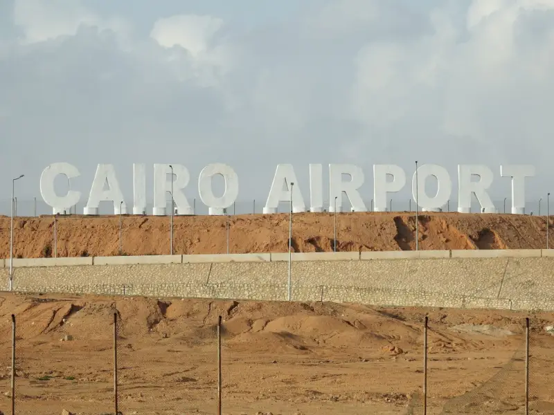 Ogromne białe litery "CAIRO AIRPORT" na tle pustynnego krajobrazu. Jedno z lotnisk w Egipcie.