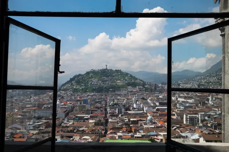 Widok na miasto z otwartego okna, z wzgórzem i pomnikiem w tle. To piękna panorama stolicy Ekwadoru, ze stolicą w Quito.