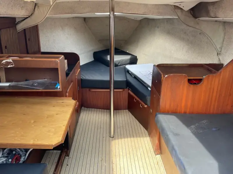 L'intérieur du Jeanneau Brio offre un espace de vie confortable avec des banquettes en tissu noir, une table en bois et des boiseries chaleureuses.