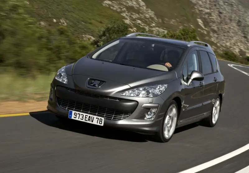 Szary Peugeot 308 2008 na krętej drodze wśród zielonych wzgórz.