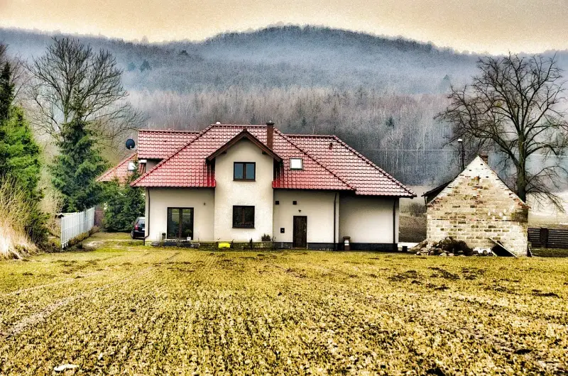 Dom z czerwonym dachem i polem przed nim. Rodzinna historia o przepisaniu domu na jedno dziecko bez zgody drugiego.