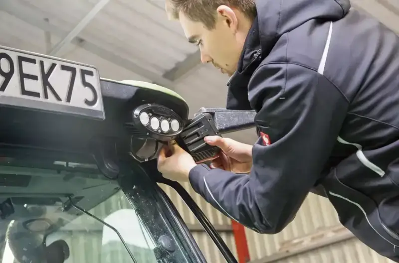 Mężczyzna dokonuje wymiany żarówki w lampie roboczej pojazdu.