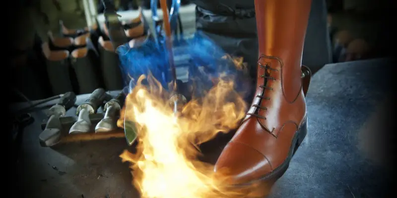 Ein brauner Reitstiefel wird mit einem Brenner bearbeitet. Werkzeuge liegen bereit für die Reitstiefel Pflege.