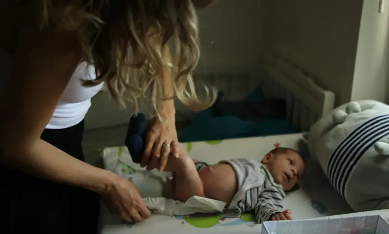 Mama zmienia pieluszkę noworodkowi. Zastanawiasz się, ile kupić pieluszek dla noworodka? Warto mieć zapas!