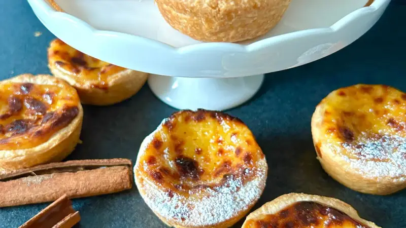 Fluffiga, gyllene pastel de nata med pudersocker och kanelstänger. En härlig fika!