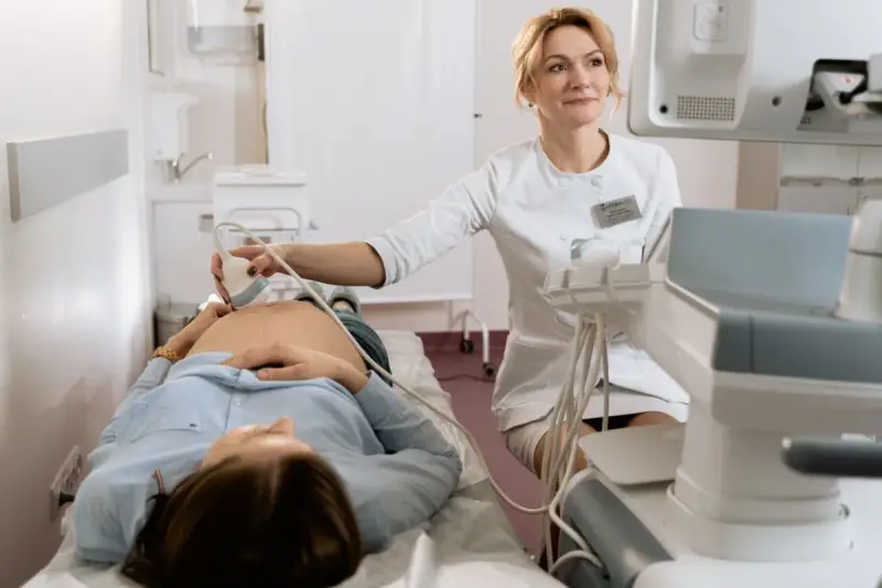 Lekarka wykonuje badania prenatalne, pokazując przyszłej mamie, jak się przygotować do wizyty.