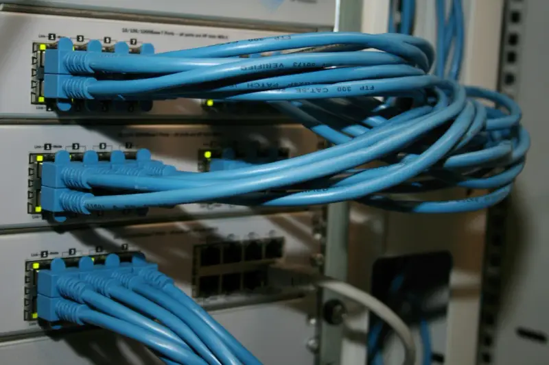 Sieć komputerowa z niebieskimi kablami Ethernet podłączonymi do przełączników. Połączenia peer to peer tworzą infrastrukturę.