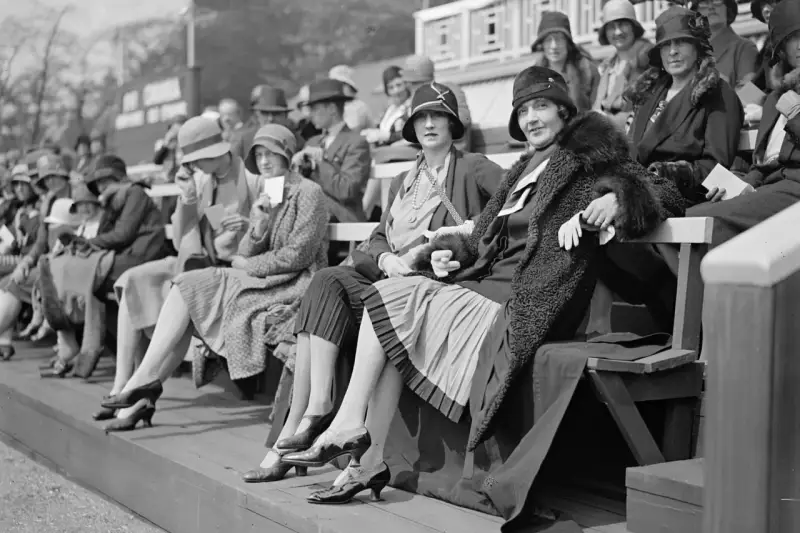 Frauen in eleganten Hüten und Kleidern, ein Bild der Weimarer Republik Mode, sitzen auf einer Tribüne.