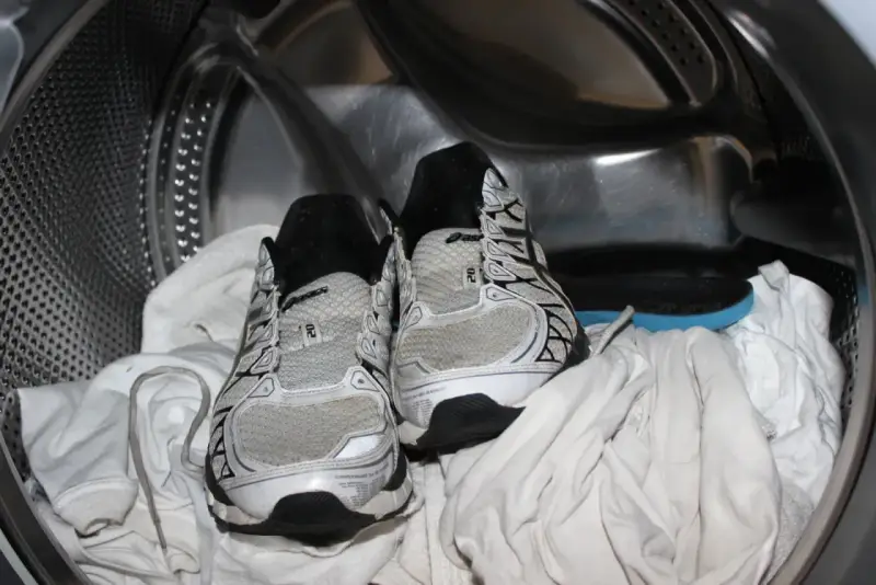 Scarpe da ginnastica pronte per essere lavate in lavatrice, insieme ad alcuni asciugamani bianchi.