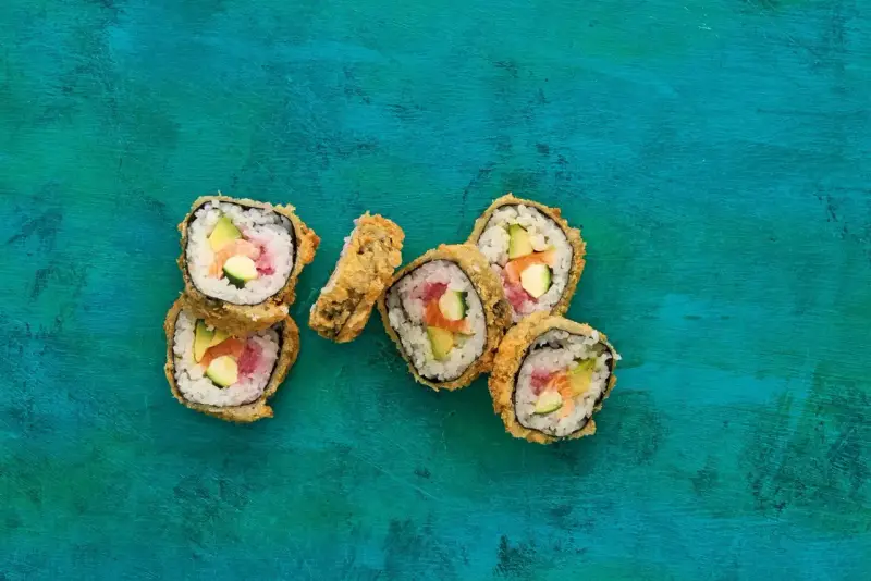 Chrupiące sushi w panko z łososiem, awokado i ogórkiem na turkusowym tle.