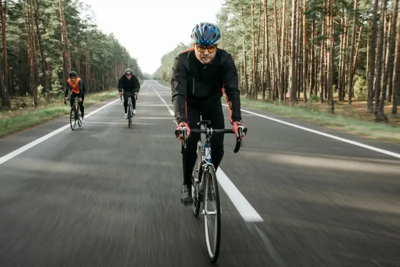 Cyclists on a road through a forest, likely engaged in a VO2 max training program, pushing their limits.