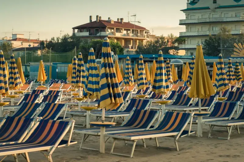 File di sdraio e ombrelloni a righe blu e gialle sulla spiaggia di Cervia Milano Marittima, pronti per accogliere i bagnanti.